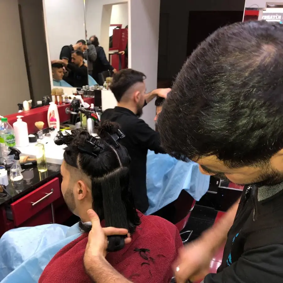 Ein Friseur arbeitet mit Haarklammern an einem Kunden, im Spiegel weitere Plätze